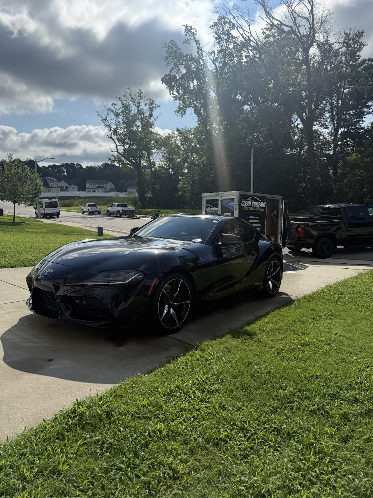 Black Toyota Supra freshly detailed in a driveway with the Clean Company Detailing trailer behind it