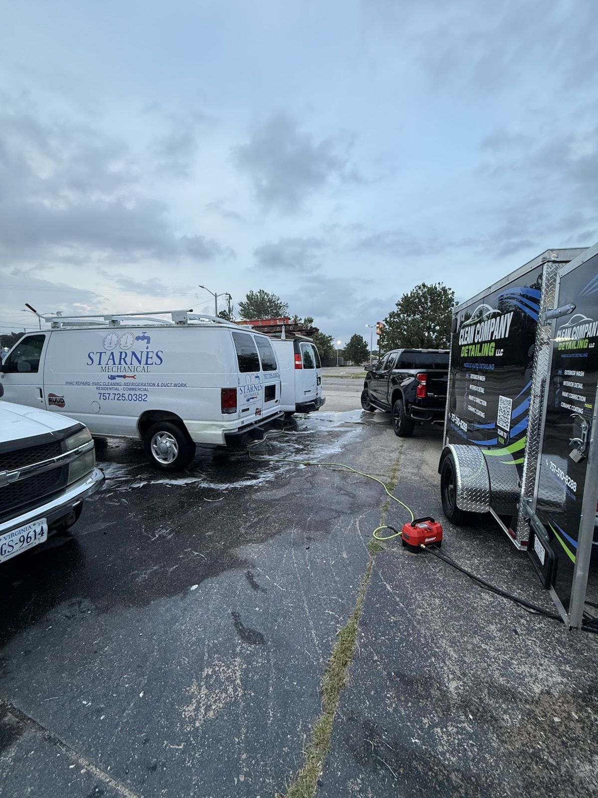 Clean Company Detailing trailer set up in a parking lot, washing a row of white service vans and a pickup on-site
